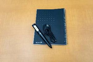 大型黑色数字笔，带有充电线和笔记本，放在桌子上